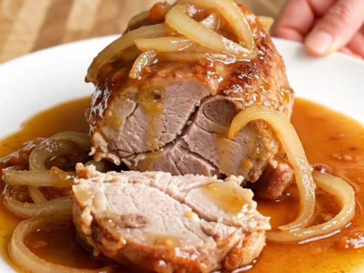 Slow cooker honey chipotle pork tenderloin with sliced onions and a glossy glaze on a white plate.