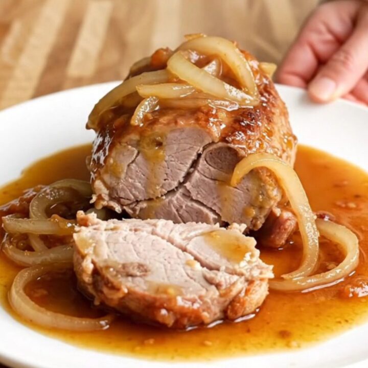 Slow cooker honey chipotle pork tenderloin with sliced onions and a glossy glaze on a white plate.