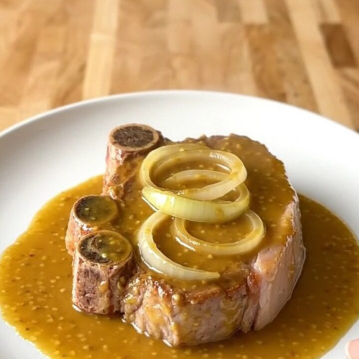 A top-down view of raw bone-in pork shoulder steaks in a white slow cooker insert with onions and sauce.