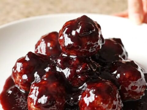 A slow cooker filled with blackberry BBQ meatballs, glistening with a dark purple glaze.