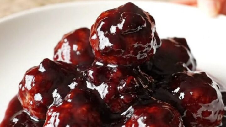 A slow cooker filled with blackberry BBQ meatballs, glistening with a dark purple glaze.