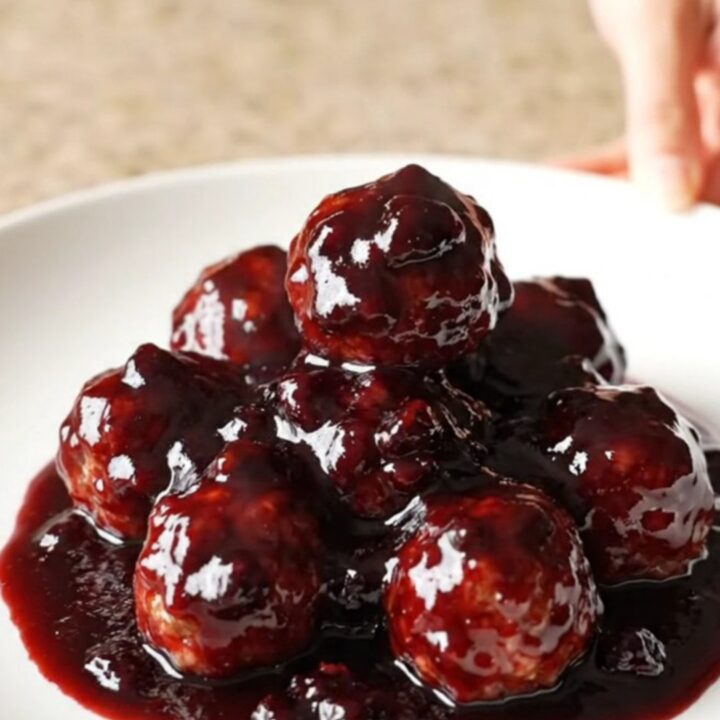 A slow cooker filled with blackberry BBQ meatballs, glistening with a dark purple glaze.