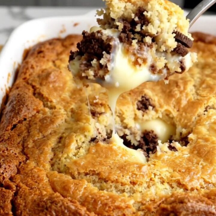 A warm, golden-brown cookies and cream dump cake in a white ceramic baking dish on a wooden countertop.
