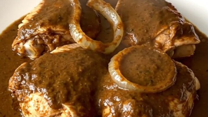 A top-down view of six raw chicken thighs in a black slow cooker insert on a speckled granite countertop.