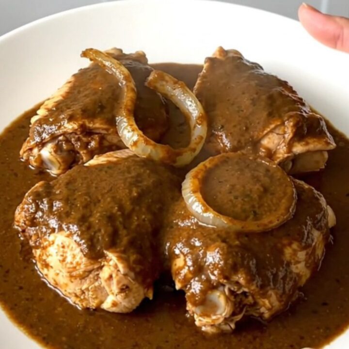 A top-down view of six raw chicken thighs in a black slow cooker insert on a speckled granite countertop.