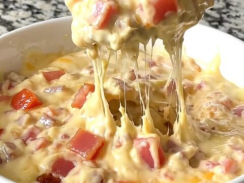 A top-down view of a black slow cooker filled with layers of bacon, diced tomatoes, and shredded cheddar cheese.
