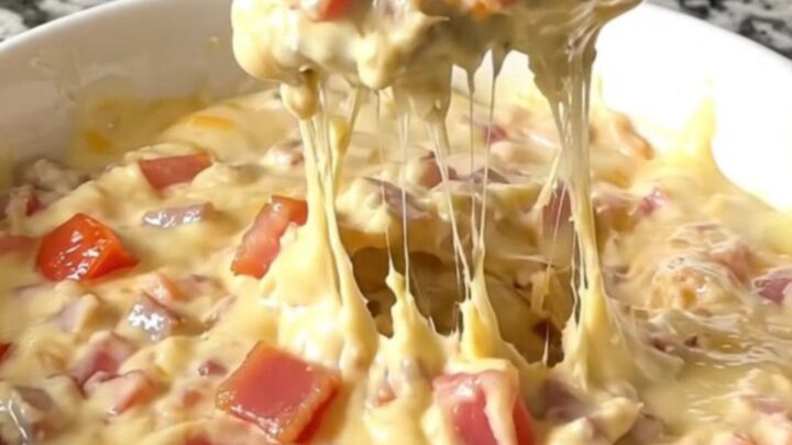 A top-down view of a black slow cooker filled with layers of bacon, diced tomatoes, and shredded cheddar cheese.