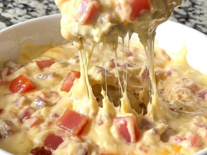 A top-down view of a black slow cooker filled with layers of bacon, diced tomatoes, and shredded cheddar cheese.
