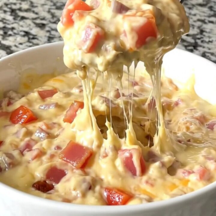 A top-down view of a black slow cooker filled with layers of bacon, diced tomatoes, and shredded cheddar cheese.