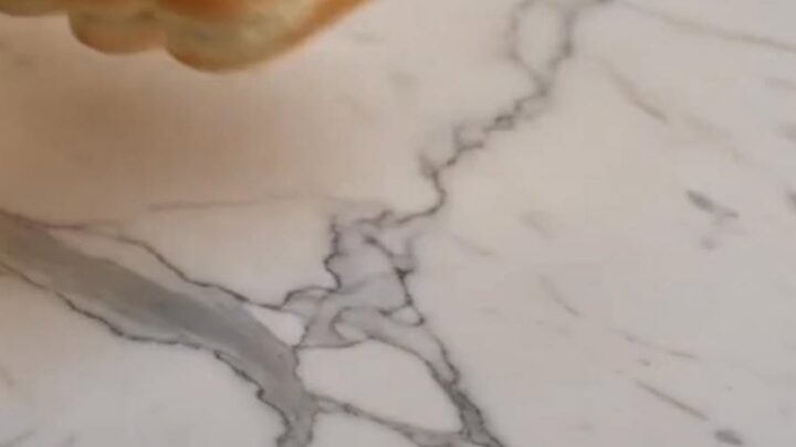 A close-up shot of a baked chili dog being pulled apart, showcasing a dramatic stretch of melted cheddar cheese and steaming