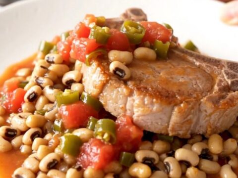 A rustic slow cooker dish featuring tender bone-in pork chops resting on a bed of savory black-eyed peas and tomatoes.