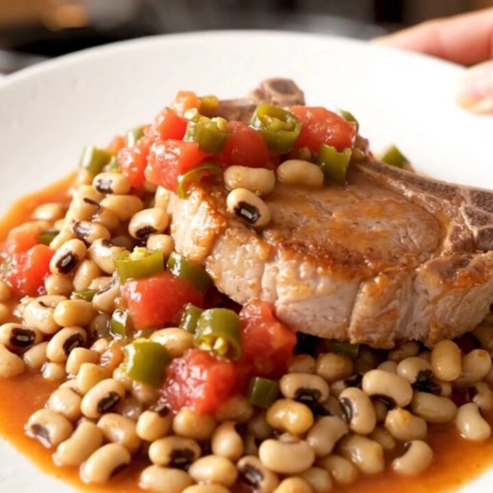 A rustic slow cooker dish featuring tender bone-in pork chops resting on a bed of savory black-eyed peas and tomatoes.
