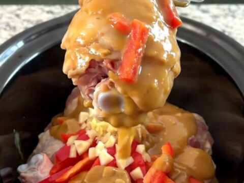 A plate of tender honey peanut chicken drumsticks covered in a rich, creamy sauce with red pepper strips.