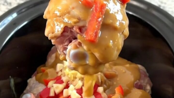A plate of tender honey peanut chicken drumsticks covered in a rich, creamy sauce with red pepper strips.