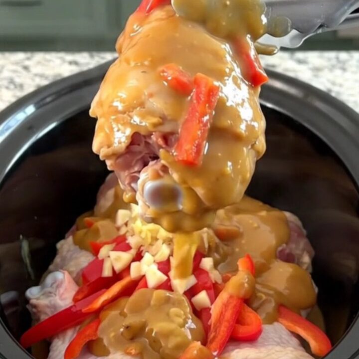 A plate of tender honey peanut chicken drumsticks covered in a rich, creamy sauce with red pepper strips.
