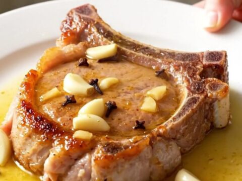 A close-up of tender, bone-in pork chops covered in a buttery garlic sauce with whole garlic cloves.
