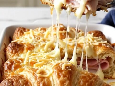 A golden, puffed Monte Cristo crescent bake in a white ceramic dish on a speckled countertop.