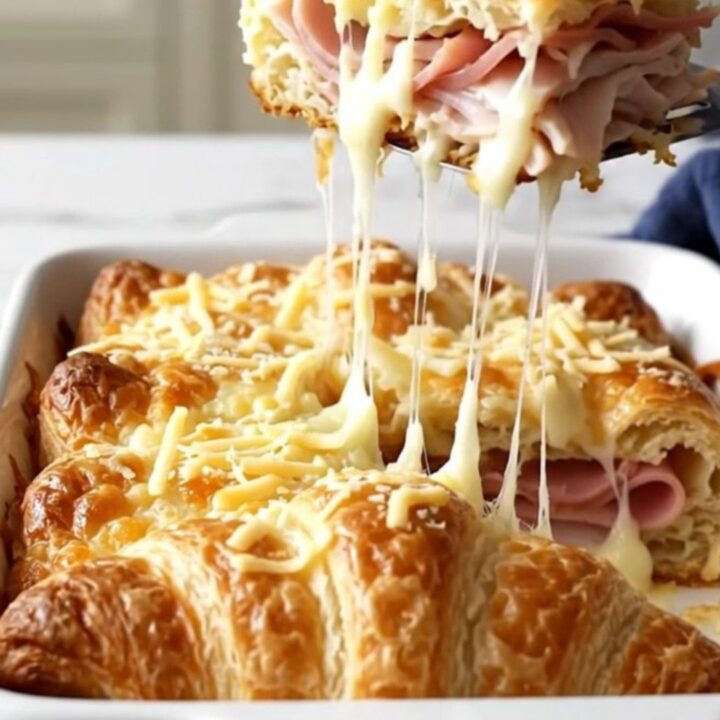 A golden, puffed Monte Cristo crescent bake in a white ceramic dish on a speckled countertop.