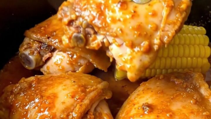 Close up of slow-cooked Cajun chicken thighs and corn cobs in a black slow cooker insert.