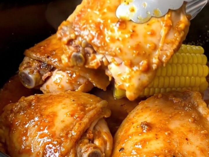 Close up of slow-cooked Cajun chicken thighs and corn cobs in a black slow cooker insert.