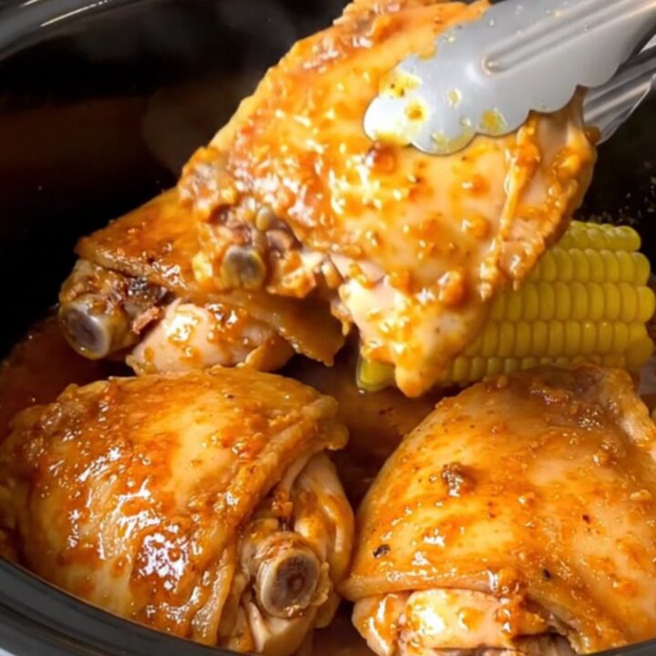 Close up of slow-cooked Cajun chicken thighs and corn cobs in a black slow cooker insert.