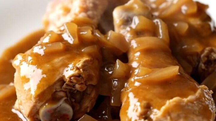 A close-up of tender, slow-cooked chicken drumsticks covered in rich brown gravy, bell peppers, and onions.