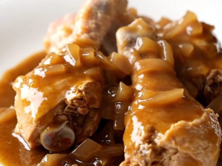 A close-up of tender, slow-cooked chicken drumsticks covered in rich brown gravy, bell peppers, and onions.