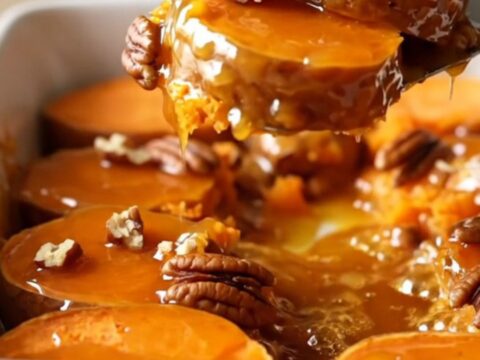 A ceramic dish filled with neatly arranged, golden-brown sweet potato rounds glazed in honey butter and topped with pecans.