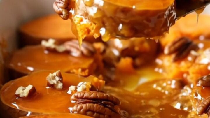 A ceramic dish filled with neatly arranged, golden-brown sweet potato rounds glazed in honey butter and topped with pecans.