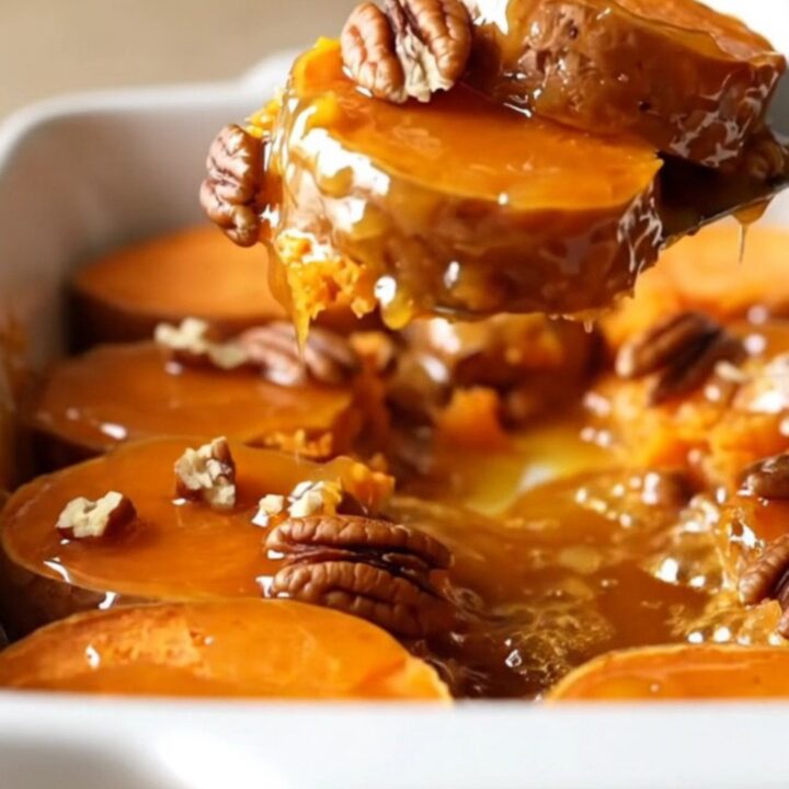 A ceramic dish filled with neatly arranged, golden-brown sweet potato rounds glazed in honey butter and topped with pecans.