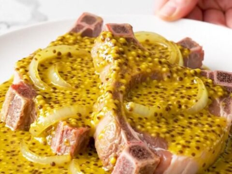 Bone-in pork chops covered in a golden mustard barbecue sauce and soft onion slices in a slow cooker.