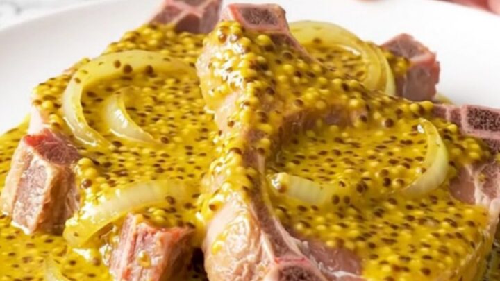 Bone-in pork chops covered in a golden mustard barbecue sauce and soft onion slices in a slow cooker.