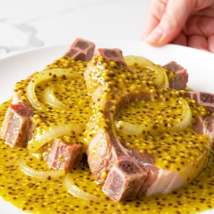 Bone-in pork chops covered in a golden mustard barbecue sauce and soft onion slices in a slow cooker.