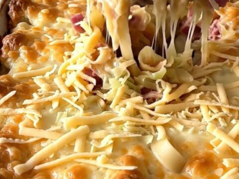 A top-down view of a Reuben noodle bake in a rectangular white ceramic dish, showing layers of noodles, corned beef