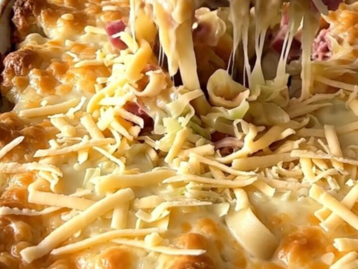 A top-down view of a Reuben noodle bake in a rectangular white ceramic dish, showing layers of noodles, corned beef