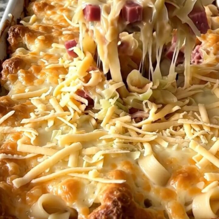 A top-down view of a Reuben noodle bake in a rectangular white ceramic dish, showing layers of noodles, corned beef