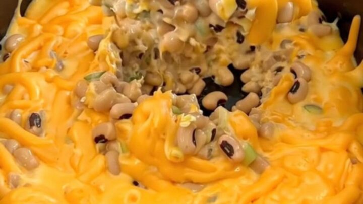 A creamy orange cheese dip with black-eyed peas, jalapenos, and green onions in a matte black slow cooker.