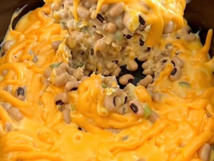 A creamy orange cheese dip with black-eyed peas, jalapenos, and green onions in a matte black slow cooker.