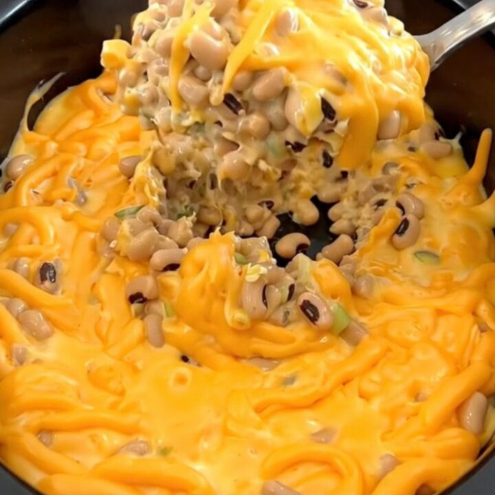 A creamy orange cheese dip with black-eyed peas, jalapenos, and green onions in a matte black slow cooker.