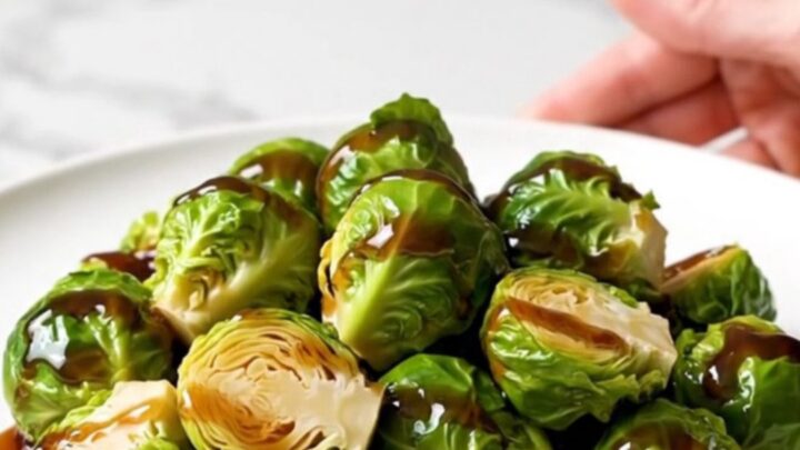 A top-down view of halved Brussels sprouts in a black slow cooker insert, seasoned and ready to cook.