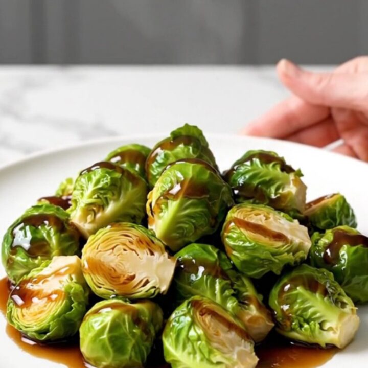 A top-down view of halved Brussels sprouts in a black slow cooker insert, seasoned and ready to cook.