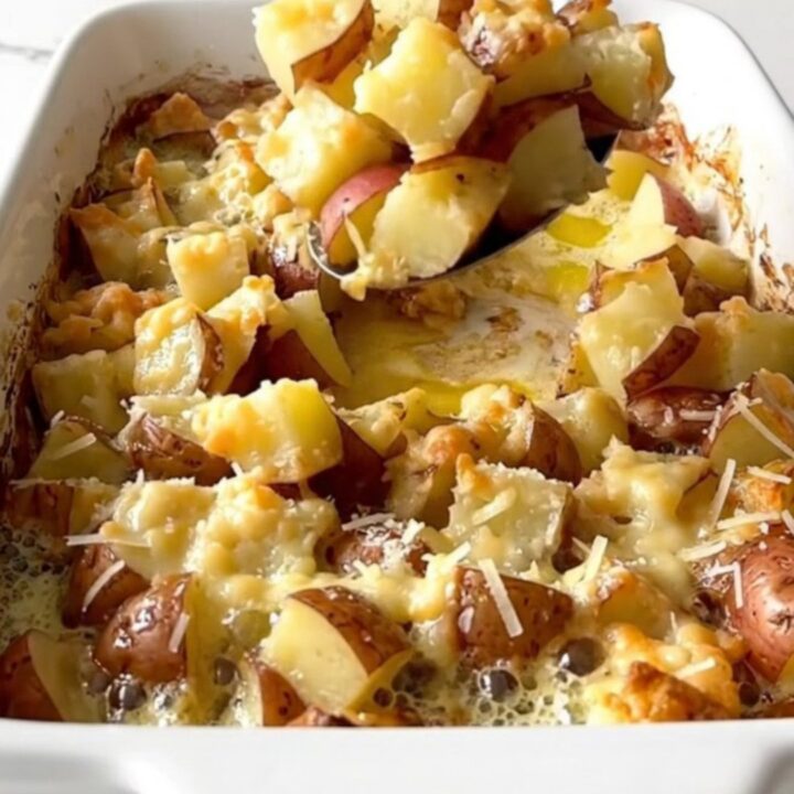 A ceramic baking dish filled with golden-brown roasted potato cubes topped with melted parmesan cheese.