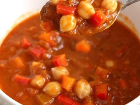 A close-up of a white bowl filled with smoky chickpea chili, featuring chickpeas and diced peppers in a thick red sauce.