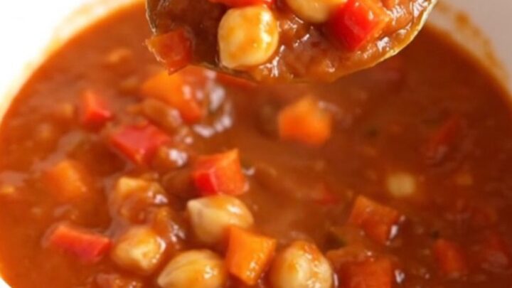 A close-up of a white bowl filled with smoky chickpea chili, featuring chickpeas and diced peppers in a thick red sauce.
