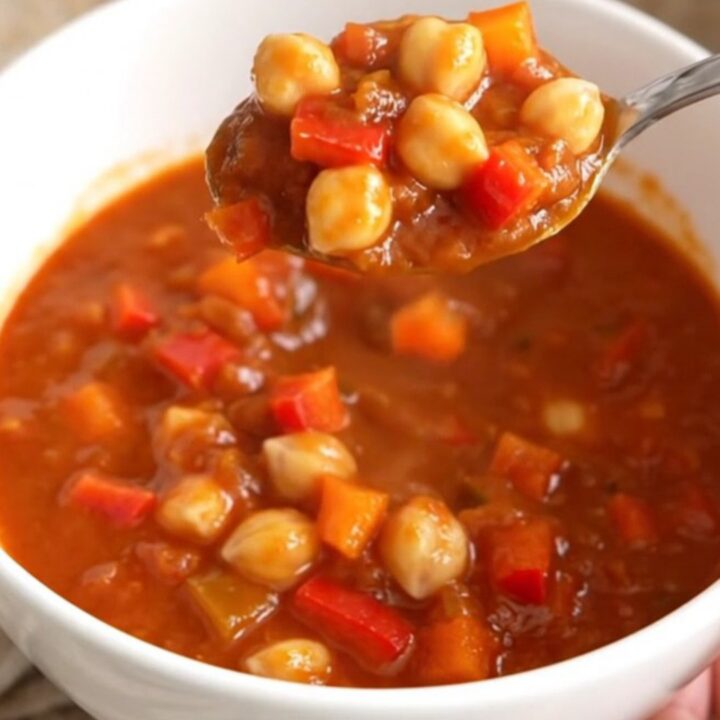 A close-up of a white bowl filled with smoky chickpea chili, featuring chickpeas and diced peppers in a thick red sauce.