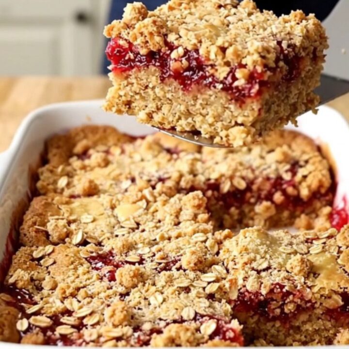 A top-down view of raspberry jam oat crumble bars in a white rectangular baking dish on a butcher-block counter.