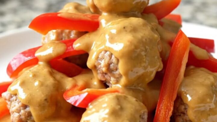 A close-up view of Thai peanut meatballs in a slow cooker, coated in a creamy sauce with red bell pepper strips.