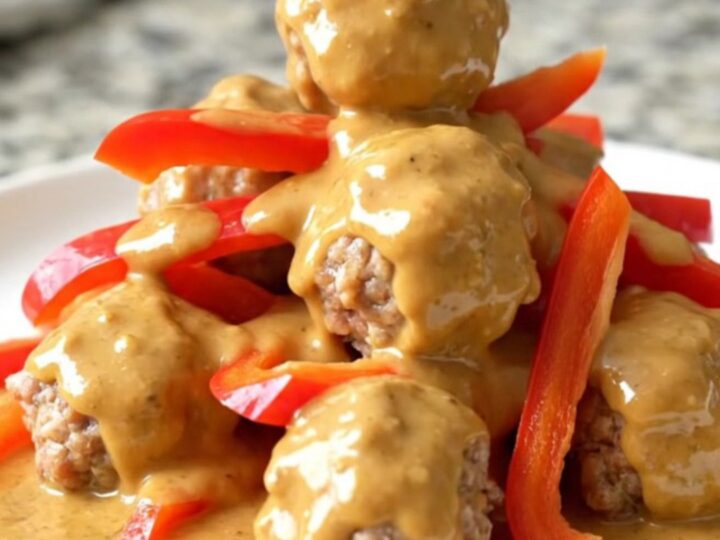 A close-up view of Thai peanut meatballs in a slow cooker, coated in a creamy sauce with red bell pepper strips.