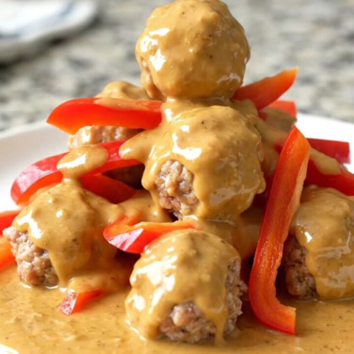 A close-up view of Thai peanut meatballs in a slow cooker, coated in a creamy sauce with red bell pepper strips.