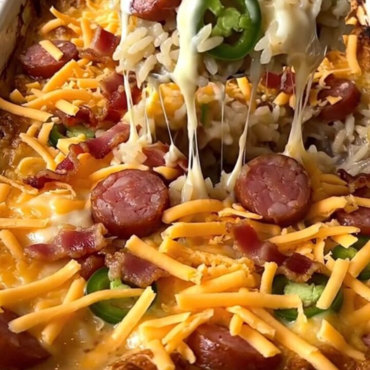 A top-down view of a creamy jalapeno popper sausage rice bake in a ceramic dish, topped with melted cheddar and bacon.
